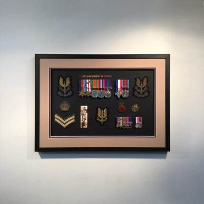 Several medals and patches arranged in a window, double mounted in a black smooth woodgrain frame