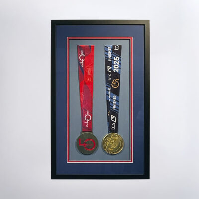 Two medals on a light blue mount, surrounded by a red and dark blue double mount in a smooth black frame